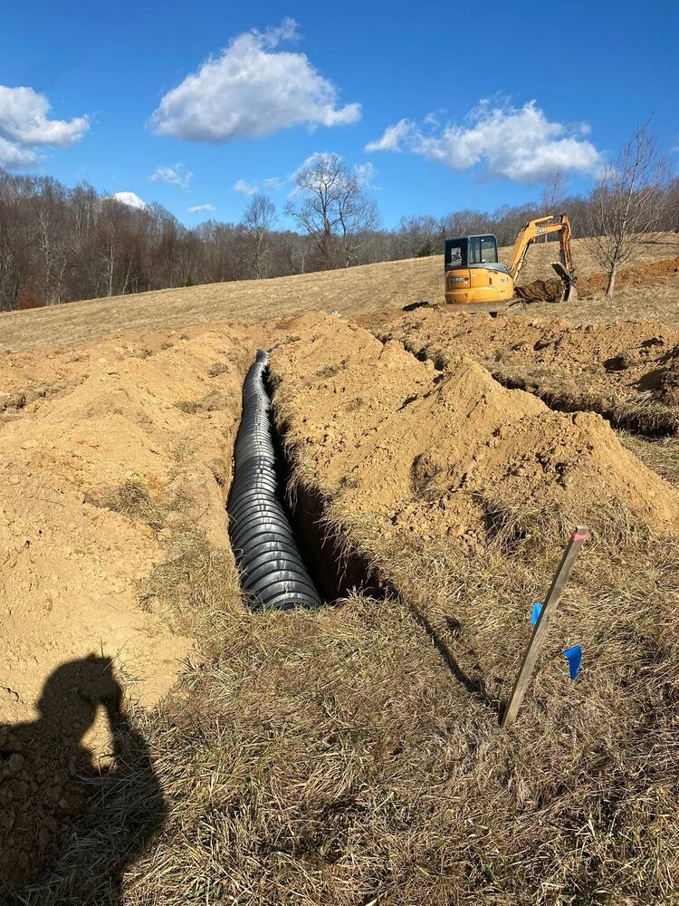 A long culvert pipe set into a trench across a field with an excavator and blue sky behind it