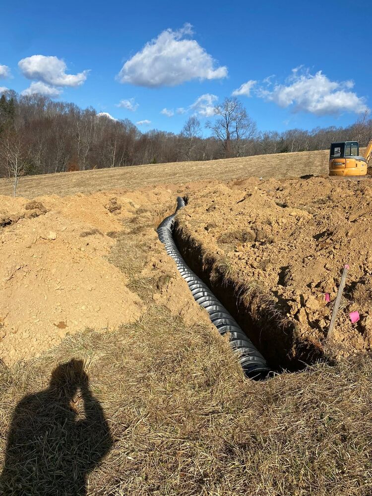 Drainage pipe laid into a trench under a bright blue sky with a machine working