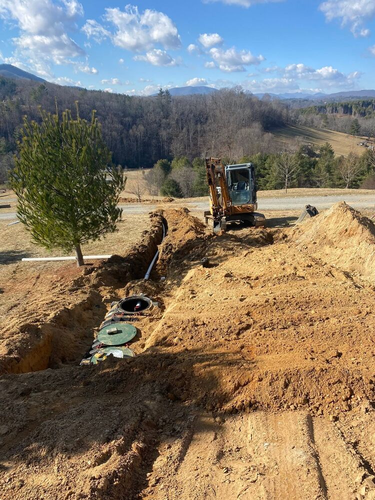 An excavator shaping a new driveway with a young tree and a mountain view behind