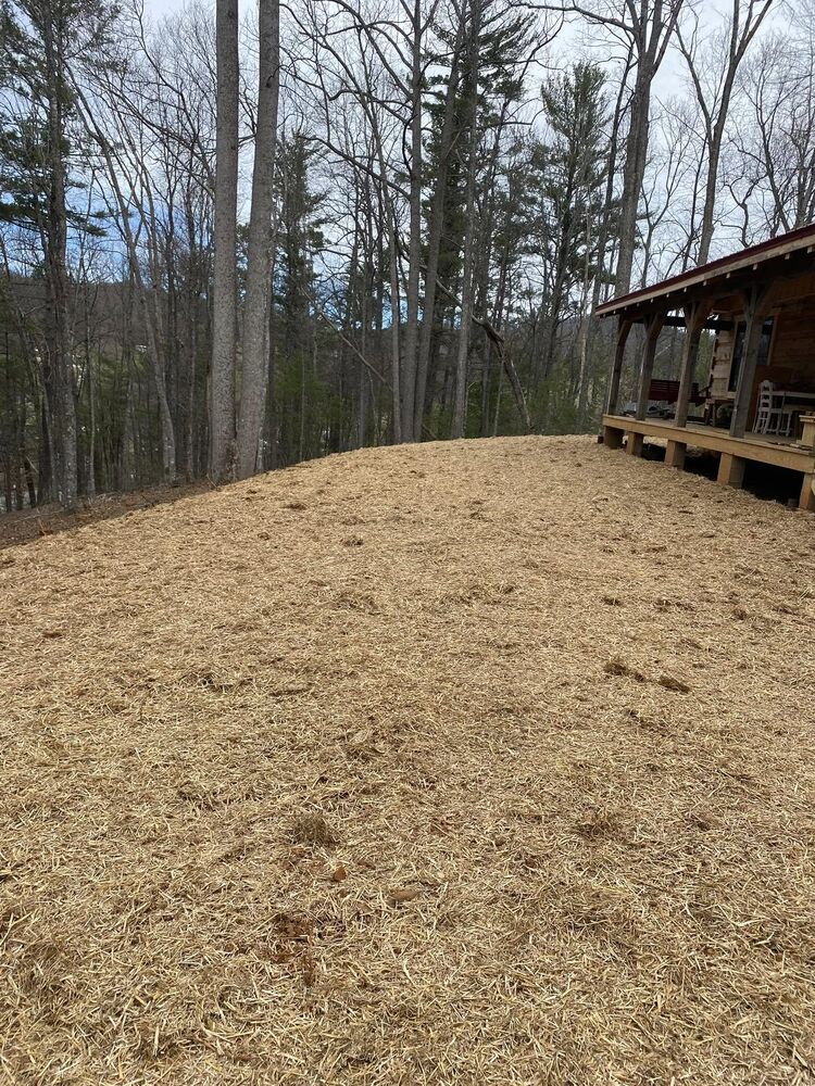 A freshly seeded and strawed slope beside a cabin porch