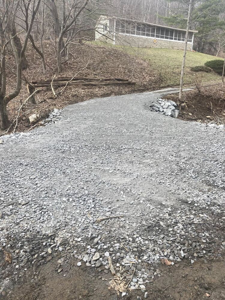 A fresh gravel drive curving toward a building at the edge of the woods