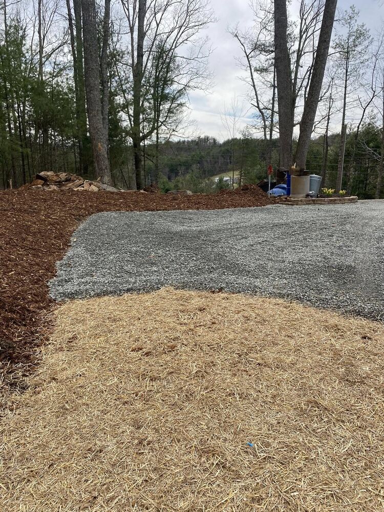 A finished gravel pad bordered by fresh mulch at the edge of a wooded mountain lot