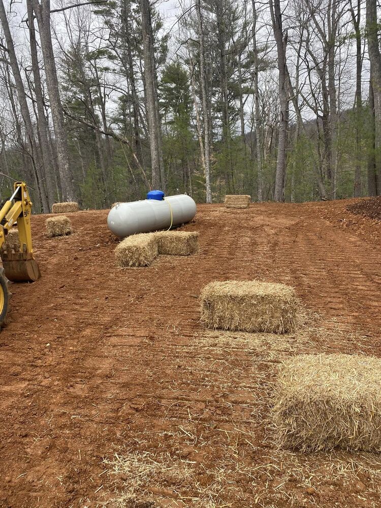 A septic tank set into graded ground with fresh straw and a machine working nearby