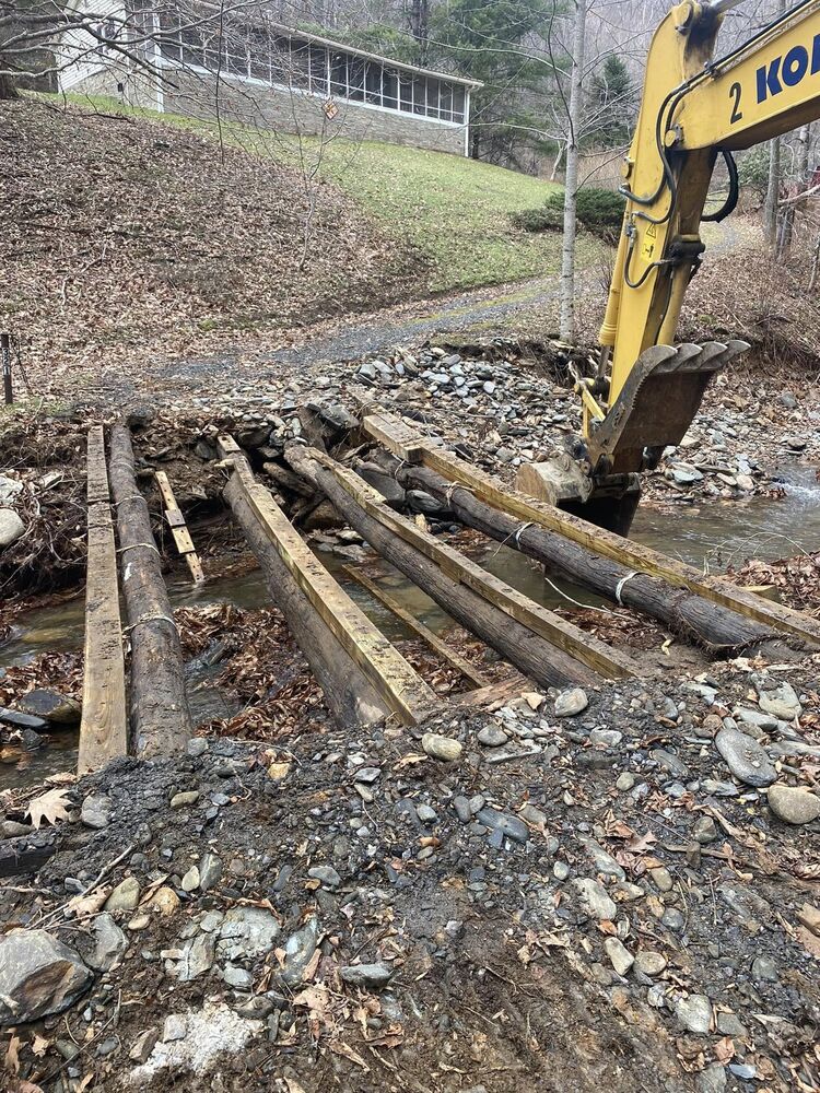 An excavator working at a timber and stone stream crossing below a house