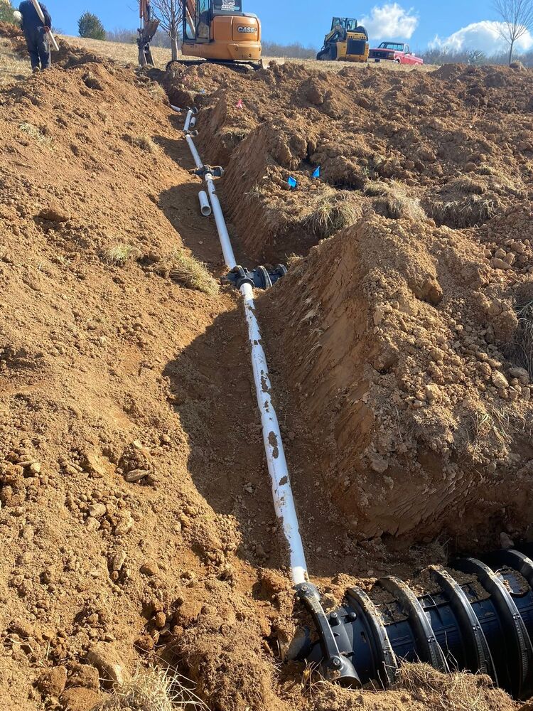 A water line being installed in a deep trench dug across a sloped lot